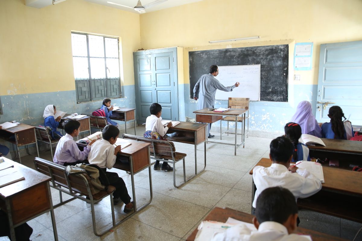 بلیک بورڈ کے پاس استاد اور توجہ سے سنتے بچے — تعلیمی وظائف کی حاضری کی شرط